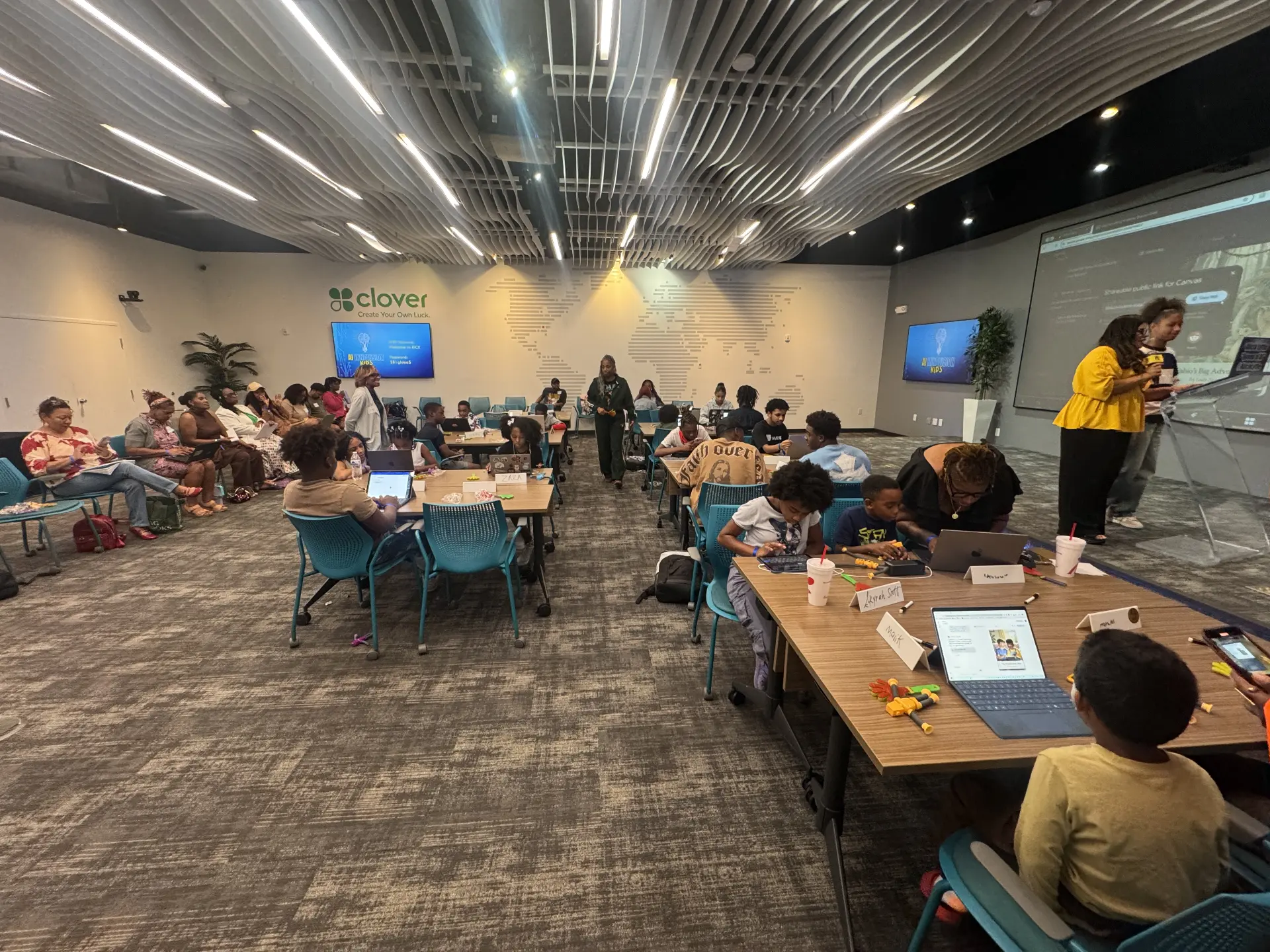Children and adults seated around workshop tables with laptops beneath a curved illuminated ceiling at the Russell Innovation Center for Entrepreneurs